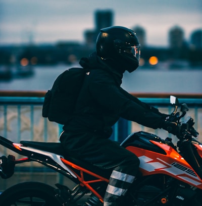 man in black jacket riding orange and black motorcycle