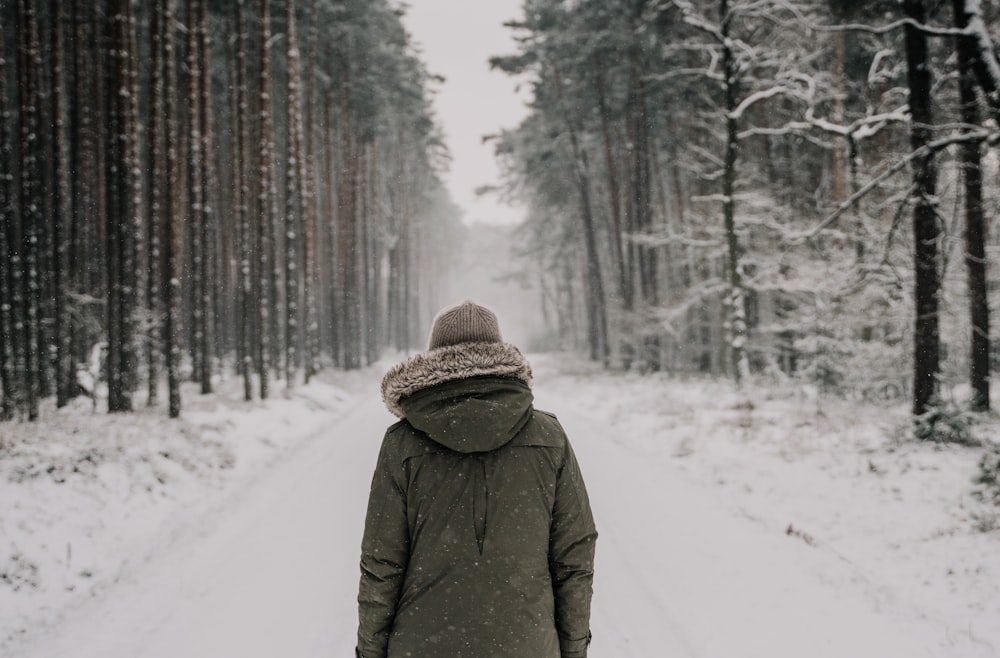 Person im schwarzen Wintermantel, die tagsüber auf schneebedecktem Boden steht