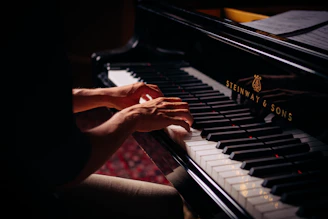Close-up of hands playing a Steinway Grand Piano under soft stage lighting.