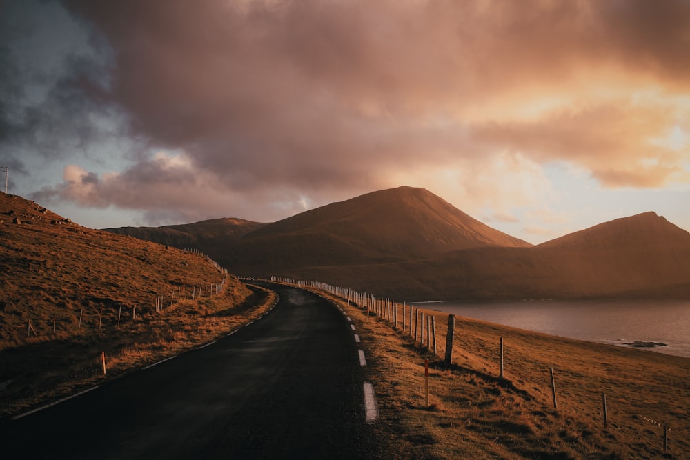 gray concrete road near mountain under cloudy sky during daytime