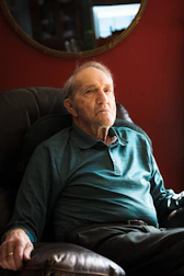 An elderly man comfortably using a home medical alert base station in his living room.