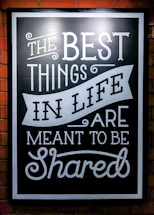 A blackboard-style sign with white decorative text stating 'The Best Things in Life Are Meant to Be Shared'. The text features various fonts and artistic flourishes, all on a black background with a white border.