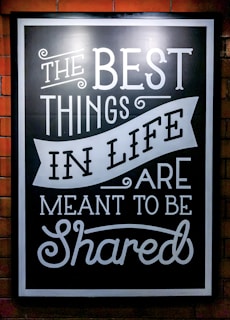 A blackboard-style sign with white decorative text stating 'The Best Things in Life Are Meant to Be Shared'. The text features various fonts and artistic flourishes, all on a black background with a white border.