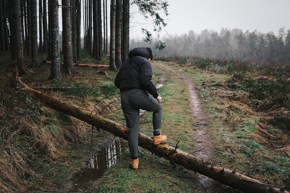 woman in black jacket and black pants walking on brown wooden log during daytime