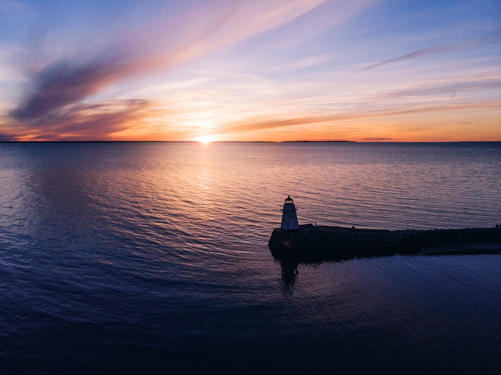 silhouette of man standing on rock in front of sea during sunset