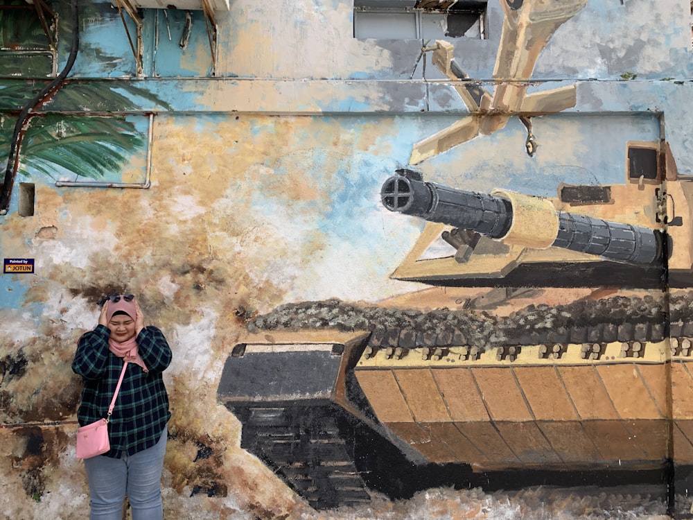 a woman standing in front of a painting of a tank