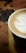 Close-up of a steaming cup of specialty coffee on a rustic wooden table with lush green coffee plants in the background.