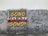 Graffiti art on a wall featuring bold text in yellow, red, and white that says 'Gomo Kelate Gomo!' with a cracked effect. Floral patterns and additional text 'Tanah Airku' are also drawn in decorative fonts on the sides. The background seems to be an old, weathered wall with some stains and cracks.