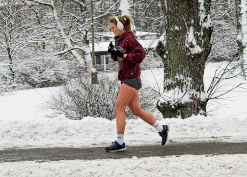 A person jogging in the park wearing lightweight, sweat-resistant earbuds.