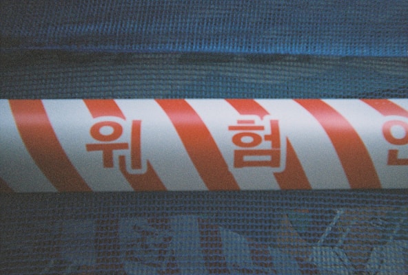 A section of a barrier tape with red and white diagonal stripes is wrapped around a textured blue surface. Korean characters are printed in red across the tape.