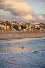 Young surfer catching a wave at sunrise near beach houses.