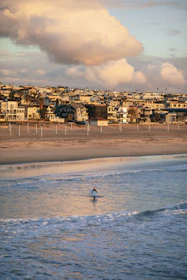 Young surfer catching a wave at sunrise near beach houses.