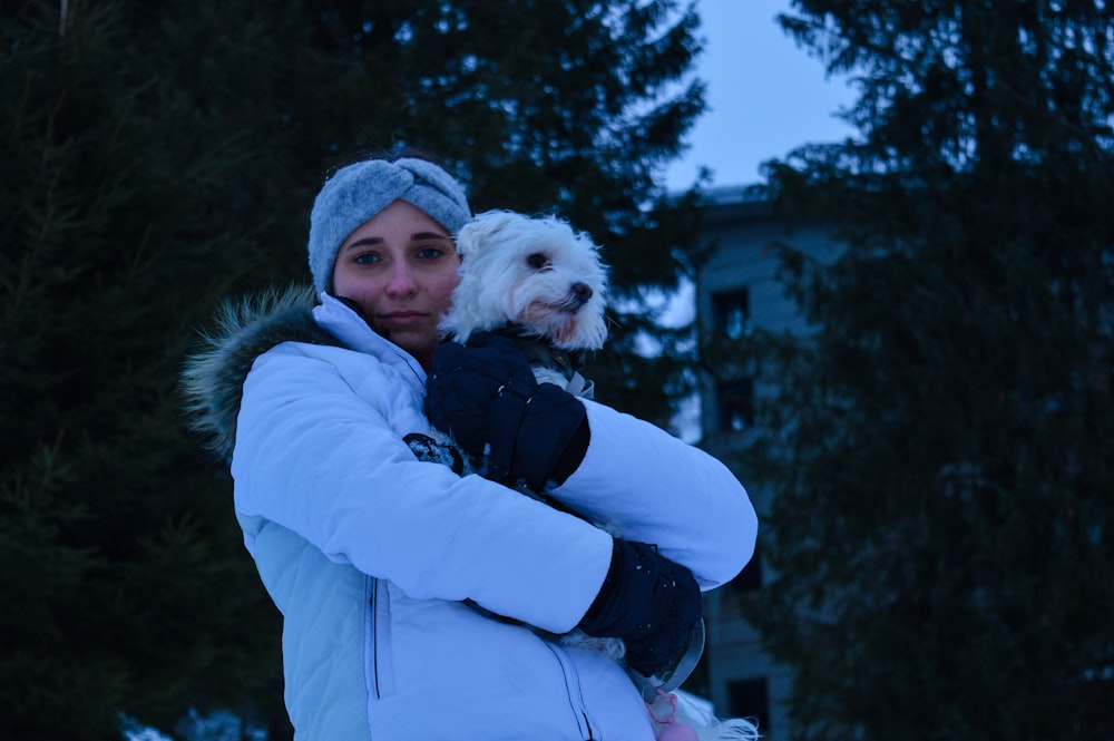 woman in blue jacket carrying white long coated dog