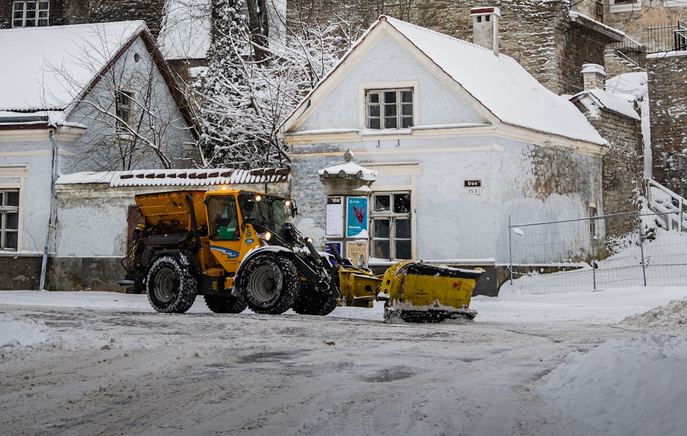 yellow and black tractor on snow covered ground near white house during daytime