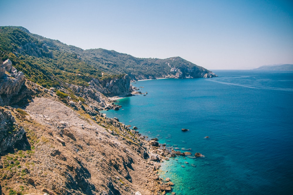 Montaña verde y marrón junto al mar azul bajo el cielo azul durante el día