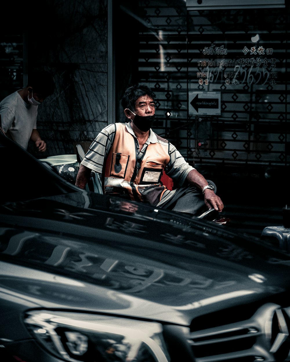 man in red and black jacket sitting on black car