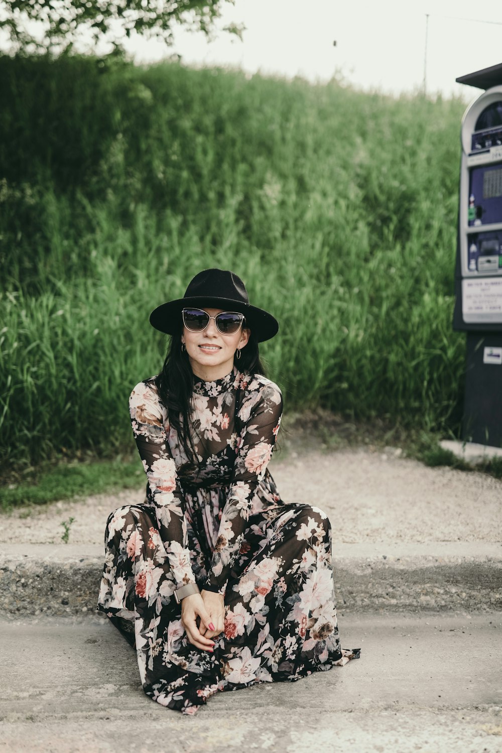 woman in black hat and brown floral dress sitting on gray concrete road during daytime