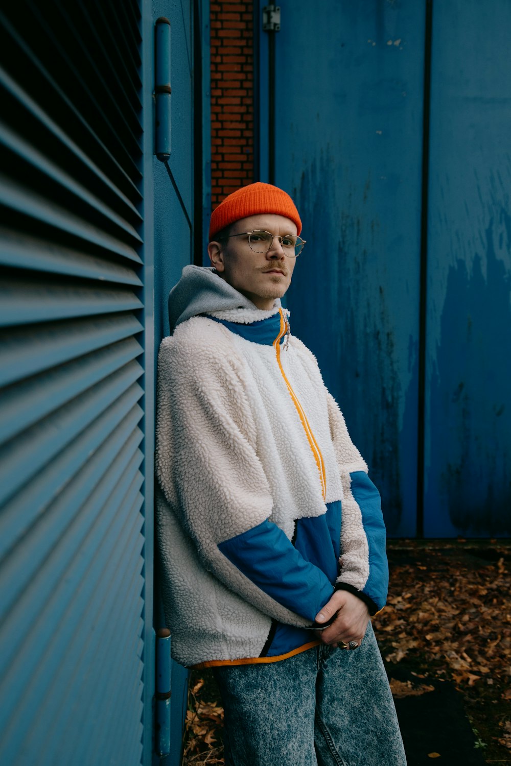 man in white and blue hoodie wearing red knit cap standing beside blue wall