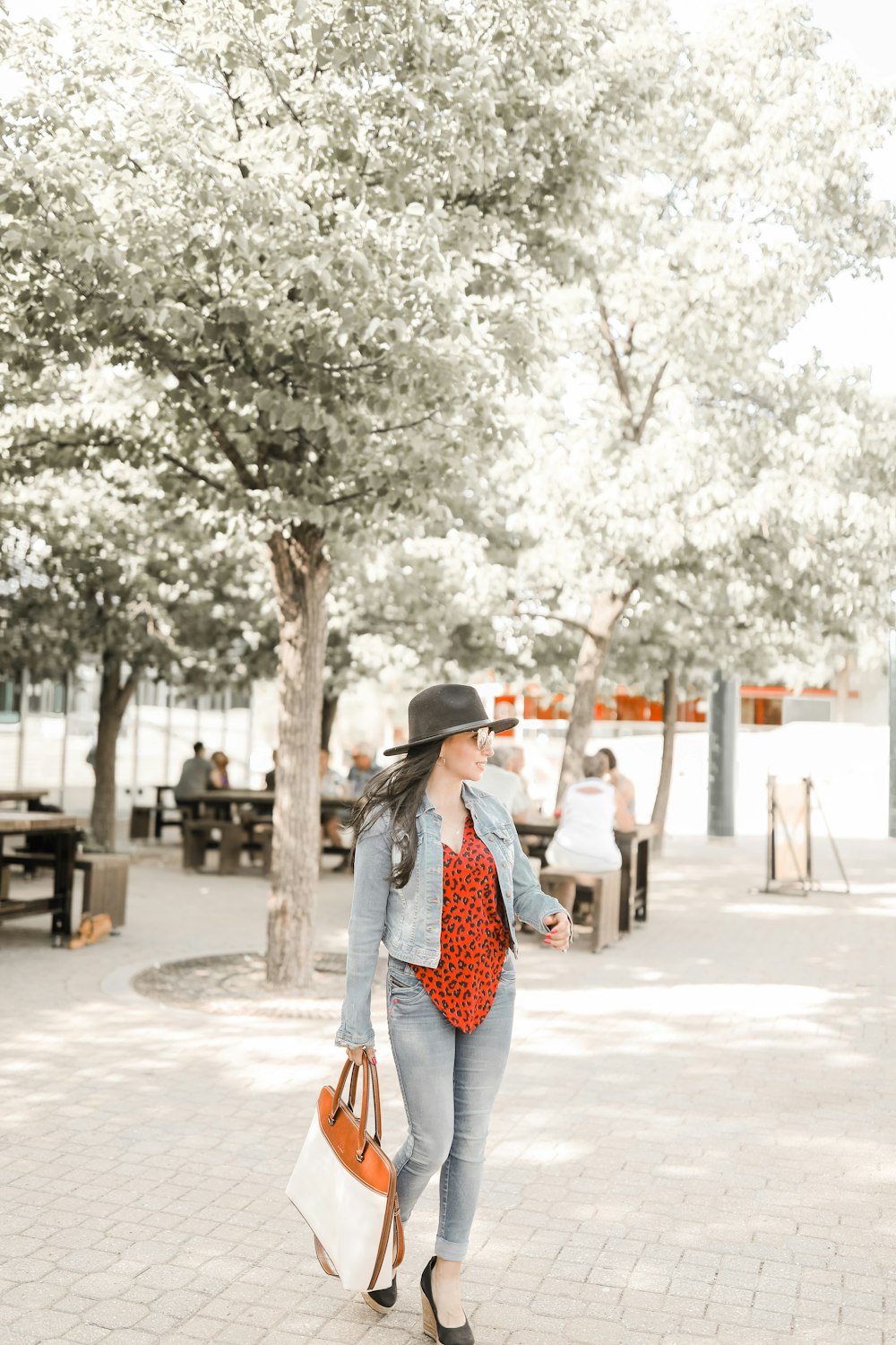 woman in white and blue polka dot dress and brown hat standing on gray concrete pavement