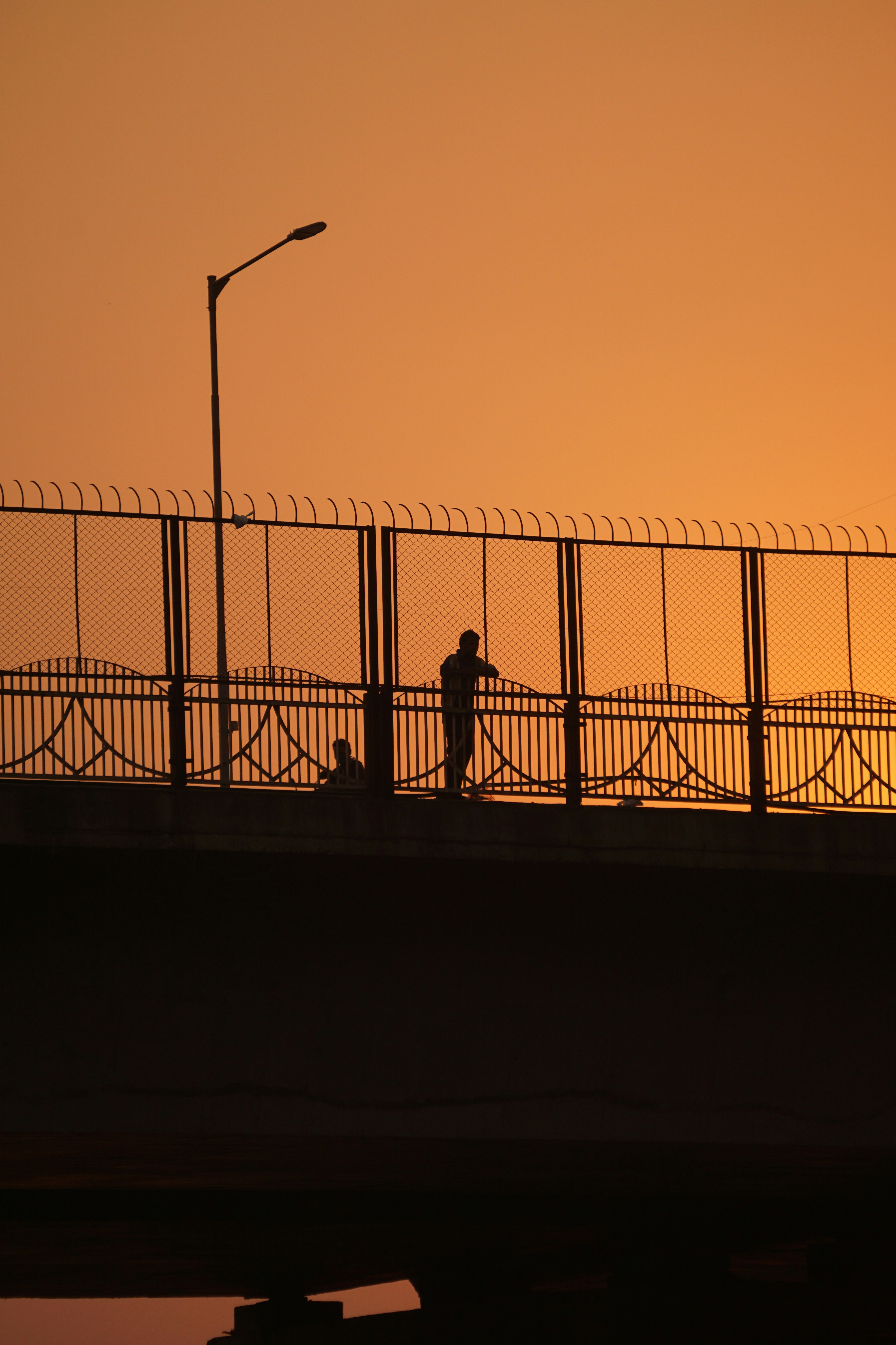 silhouette of 2 person standing beside fence during sunset