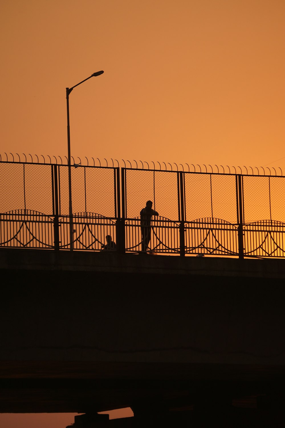 silhouette of 2 person standing beside fence during sunset