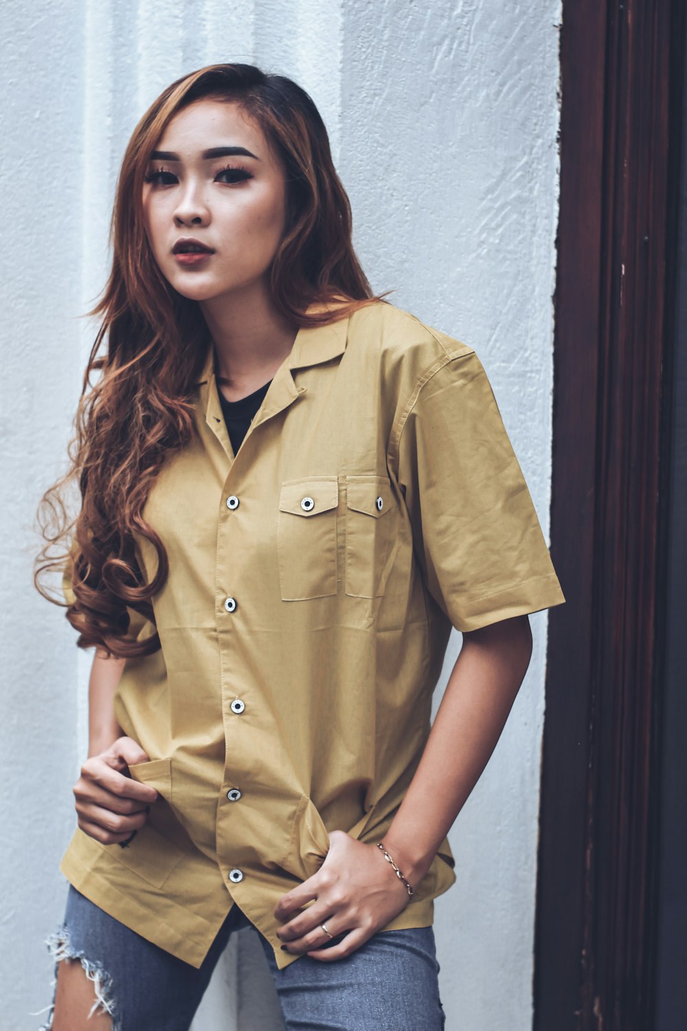 woman in yellow button up shirt leaning on white wall