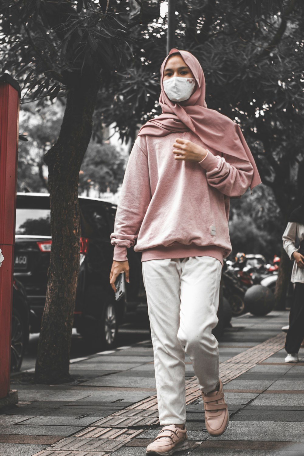 uomo in felpa con cappuccio rosa e pantaloni grigi in piedi sul marciapiede durante il giorno