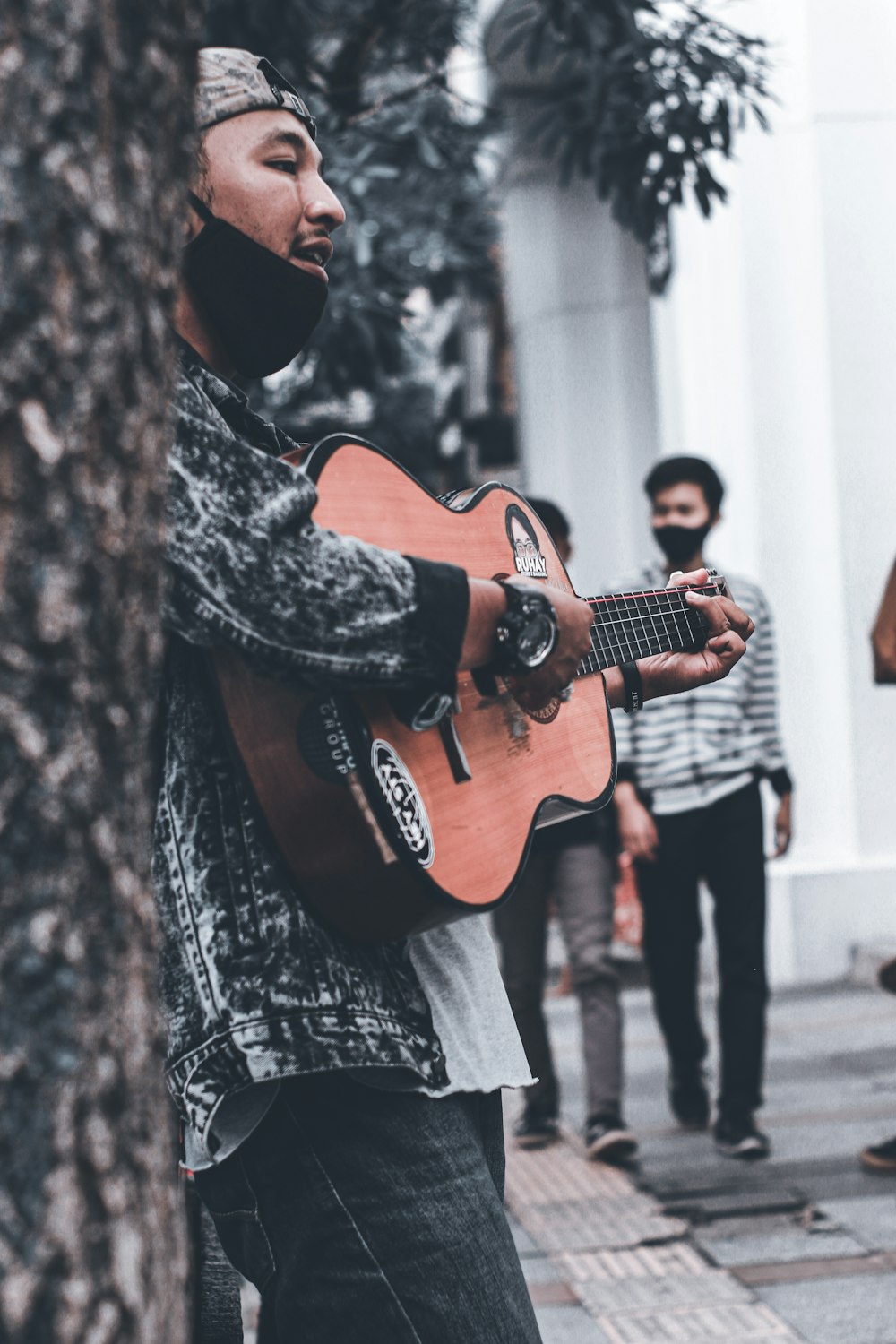homme en manteau noir et blanc jouant de la guitare acoustique marron
