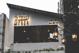 A small establishment with a sign reading 'Teras Braga' and 'est. 2020' on its exterior. The modern design features a partially covered seating area with hanging lamps. A vintage-style street lamp adds to the ambiance.