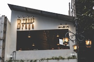A small establishment with a sign reading 'Teras Braga' and 'est. 2020' on its exterior. The modern design features a partially covered seating area with hanging lamps. A vintage-style street lamp adds to the ambiance.
