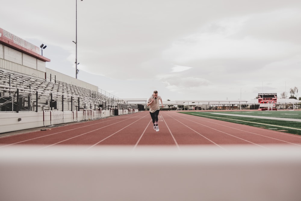 Donna in camicia nera a maniche lunghe e pantaloni neri che corre sul campo di atletica durante il giorno