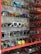 A collection of various sunglasses displayed on multiple glass shelves, featuring a range of colors and styles. The frames vary from modern and sleek to retro and bold designs, with lenses that are tinted in different hues such as blue, gold, and dark shades.