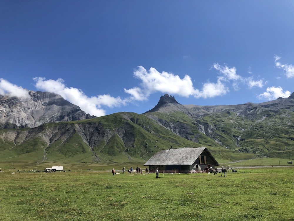 casa de madeira marrom no campo de grama verde perto da montanha sob o céu azul durante o dia