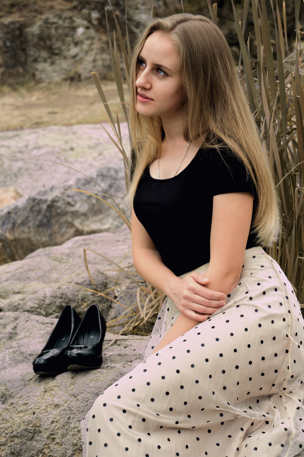 woman in black tank top and white polka dot pants sitting on rock