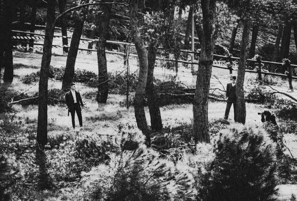 grayscale photo of 2 person standing near trees