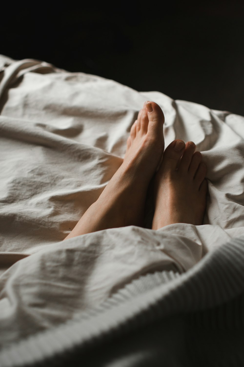 person in gray sweater lying on white bed