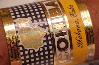 A close-up of a cigar band with 'Cohiba' prominently displayed, featuring a black and white checkered pattern accented with gold and yellow details. The words 'Habana, Cuba' are elegantly scripted on the band.