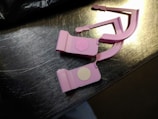 Two pink plastic clips with circular adhesive pads are placed on a metallic surface. The surface reflects light, showing a shiny appearance.