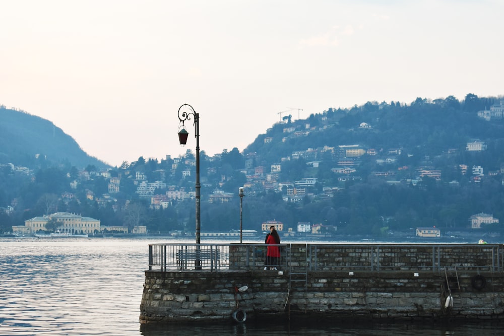 person in red jacket standing on concrete dock during daytime