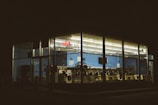 A laundromat is illuminated at night, visible from outside through large glass windows. The interior features rows of washing machines and dryers, and the walls are painted blue. An 'Open' neon sign is glowing inside.