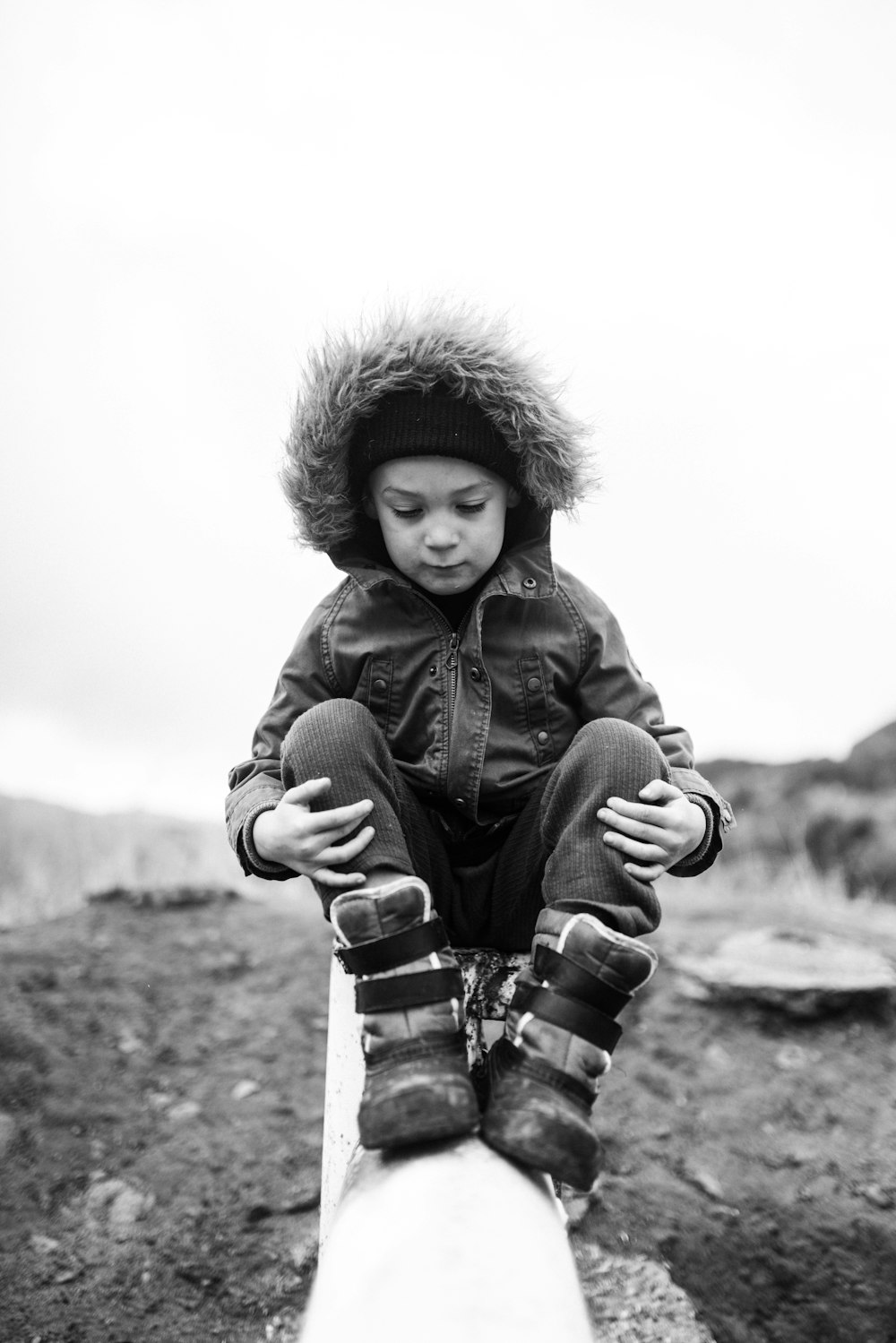 grayscale photo of girl in jacket and boots sitting on ground