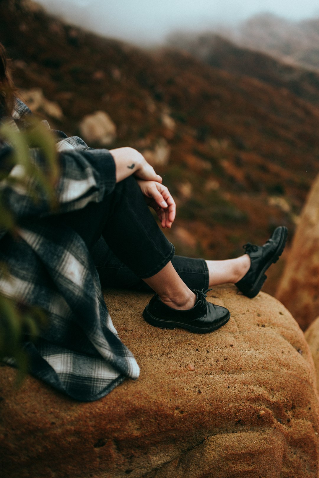 person in black pants and black shoes sitting on brown rock during daytime