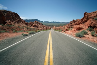 gray concrete road between brown mountains under blue sky during daytime