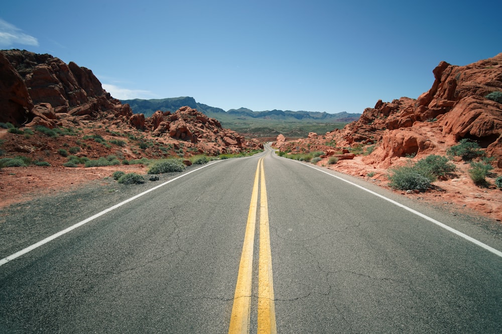 gray concrete road between brown mountains under blue sky during daytime