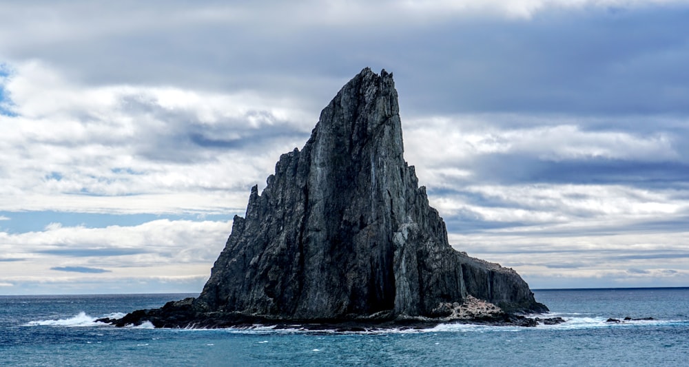 Formación rocosa gris en el mar azul bajo nubes blancas durante el día