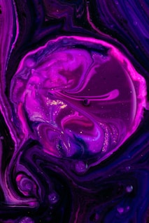 Swirls and patterns of vibrant magenta and purple hues create a mesmerizing abstract design, resembling a cosmic or galactic scene. There are hints of glittery highlights adding a touch of sparkle and depth.