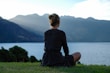 a woman sitting on the grass looking out over a lake