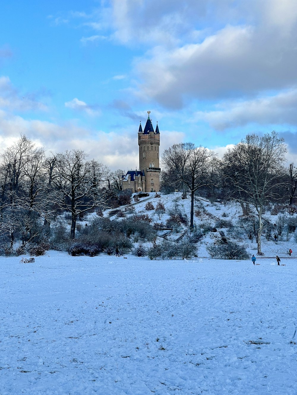 brown concrete building surrounded by snow covered trees under blue sky and white clouds during daytime