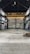 An empty industrial warehouse with high ceilings and large metal beams. The space is spacious with concrete floors and walls that show signs of wear, offering a gritty and raw aesthetic. Overhead, a big yellow crane is installed, indicating the space's potential for lifting heavy materials.