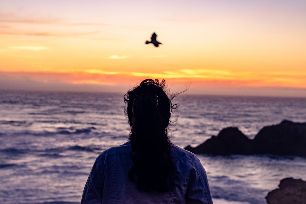 woman in gray shirt standing near sea during sunset